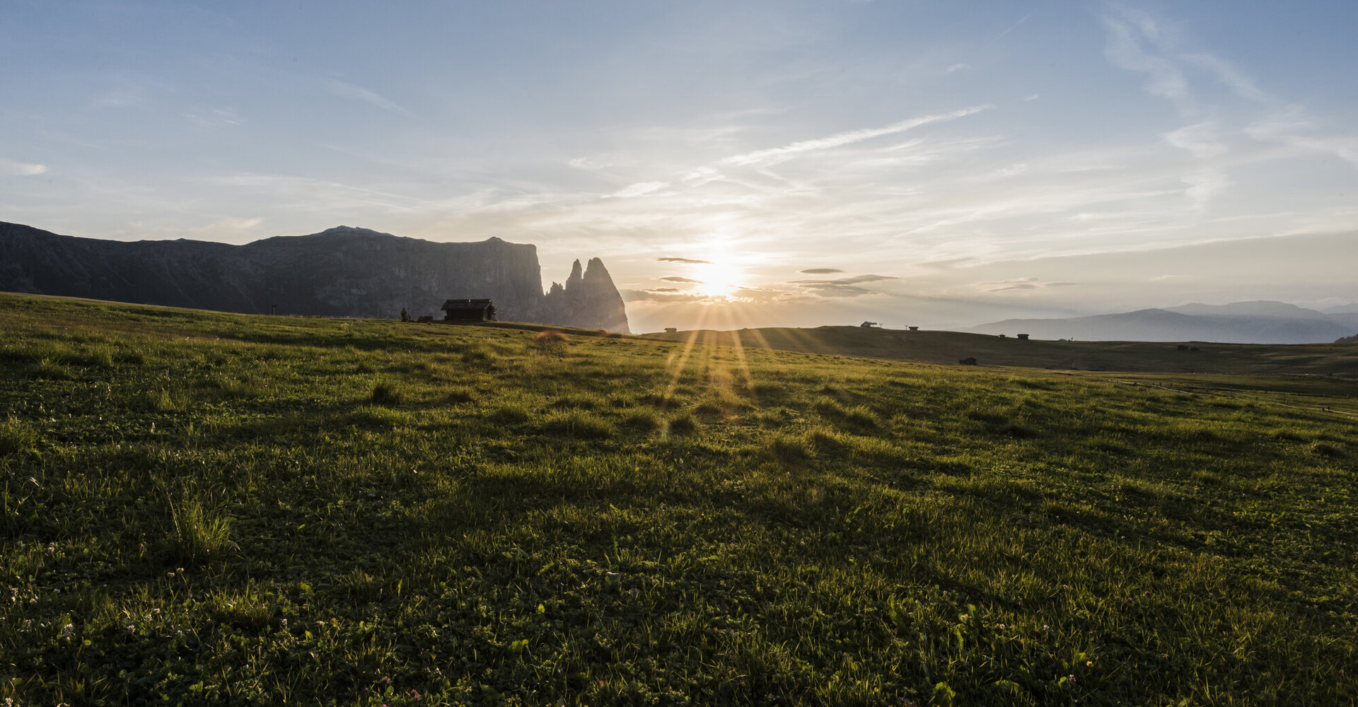 Sonnenuntergang über den Schlern in den Dolomiten mit orange leuchtenden Felsen und Almwiesen im Vordergrund