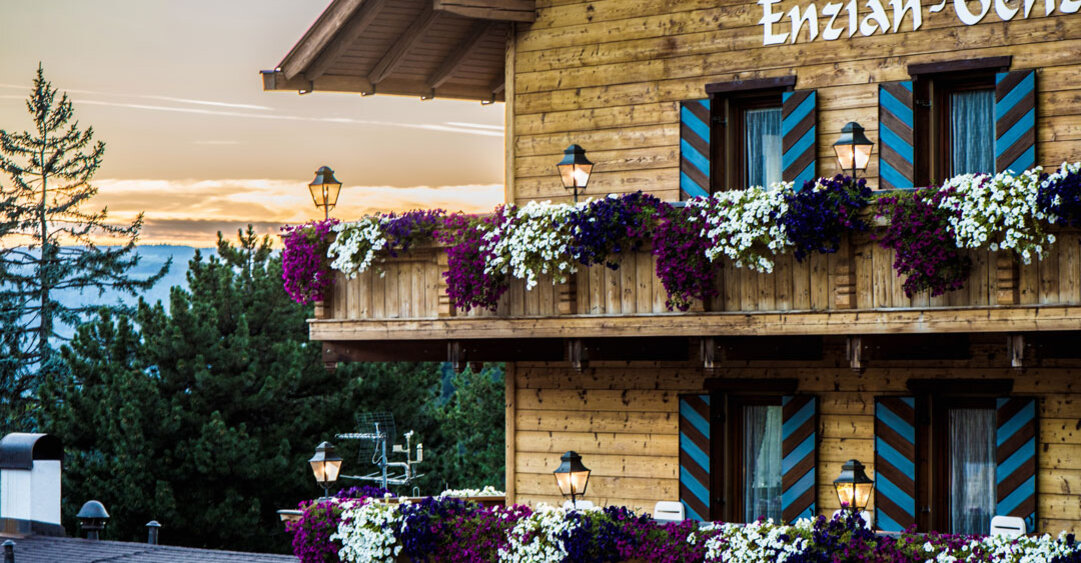 Hoteleingang mit blumengeschmückten Balkonen, Holzfassade und beleuchtetem Hotelschild im Abendlicht