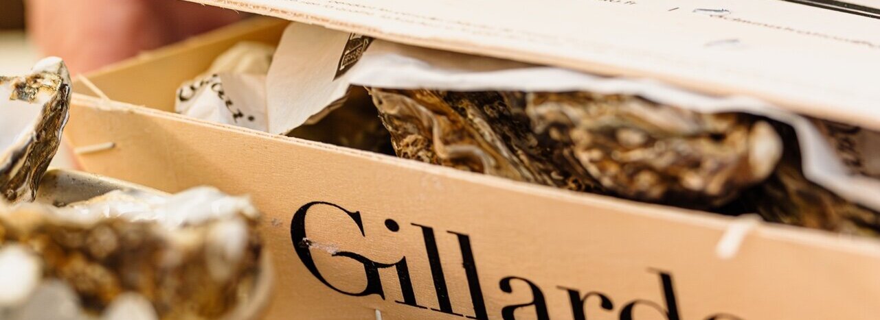 Wooden board with an open Gillardeau box and fresh oysters on a wooden table